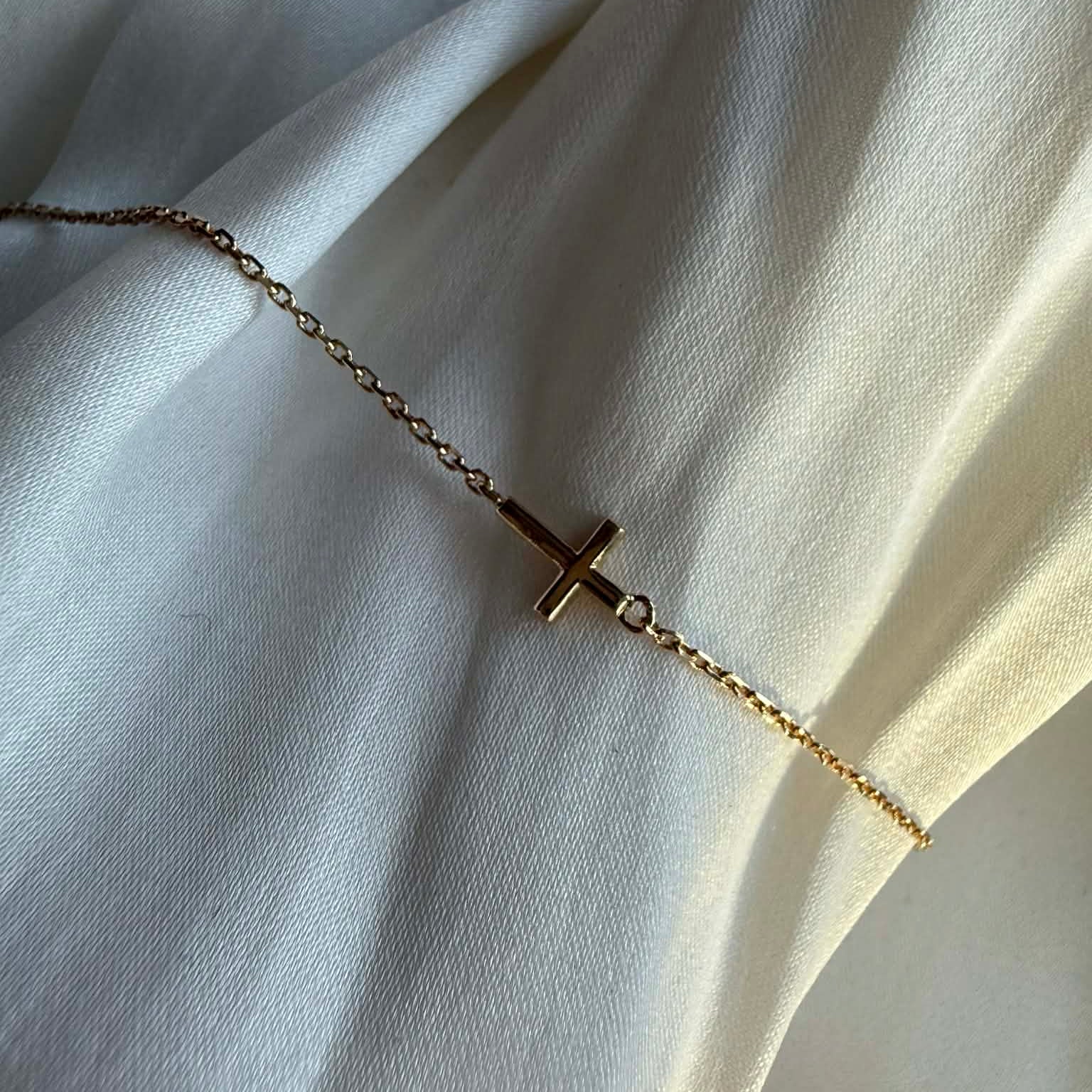 Kors armbånd i 18 kt guld - close up vist på klæde